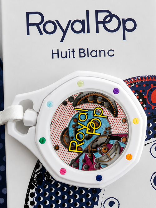 A close-up of a Royal Pop Huit Blanc wristwatch with a white case and colorful pop-art dial, resting on its branded packaging box.