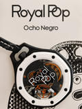 A close-up of a Royal Pop Ocho Negro watch with a black case, white bezel, and skeletonized dial showing orange and silver gears. The watch is displayed on a light beige background with a black-and-white patterned prop and the text 'Royal Pop Ocho Negro' printed on the left.