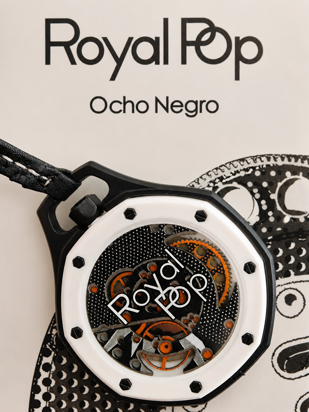A close-up of a Royal Pop Ocho Negro watch with a black case, white bezel, and skeletonized dial showing orange and silver gears. The watch is displayed on a light beige background with a black-and-white patterned prop and the text 'Royal Pop Ocho Negro' printed on the left.